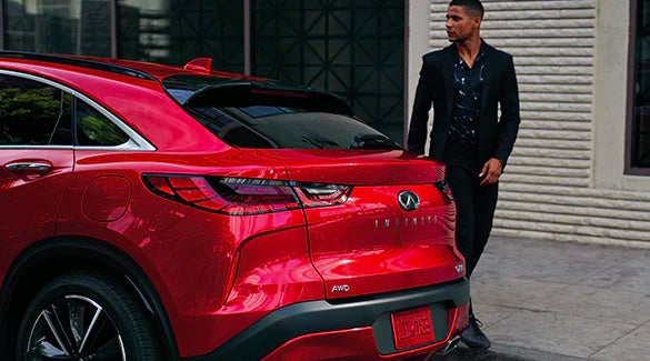 Man walking behind a red INFINITI QX55 Crossover Coupe SUV parked on street